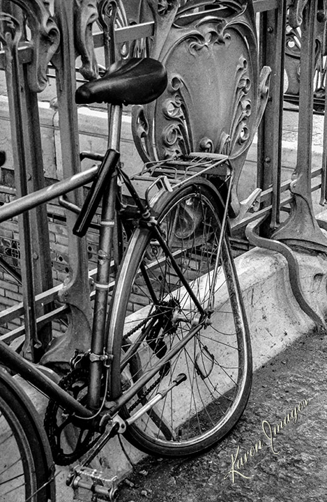 A black and white image of fine art photography of a bicycle locked to a metro station entrance in Paris France photographed by Atlanta Fine Art Photographer Karen Images