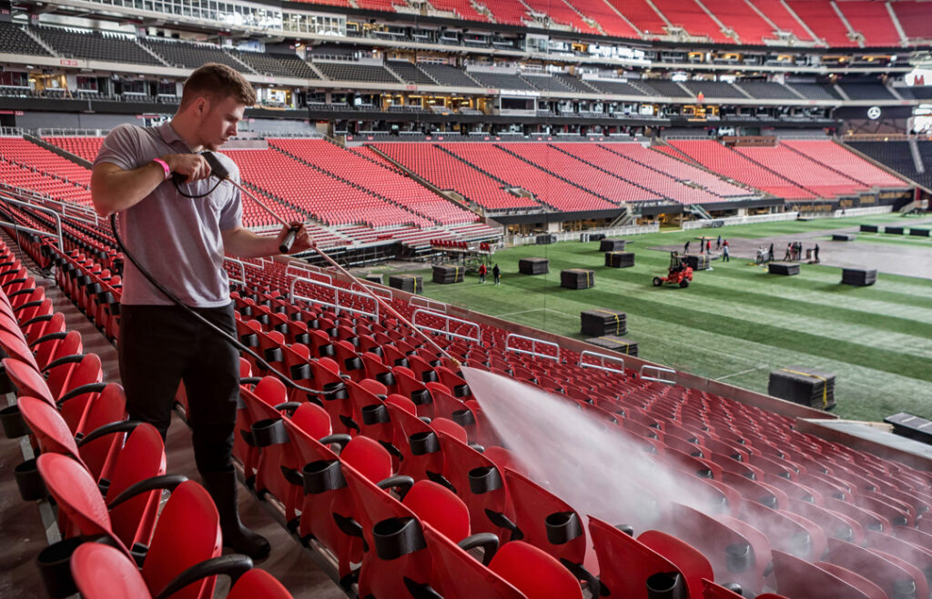 A custom stock image of a Level 7 Facilities Services employee pressure washing seats in Mercedes Benz Stadium by Atlanta Commercial Photographer Karen Images