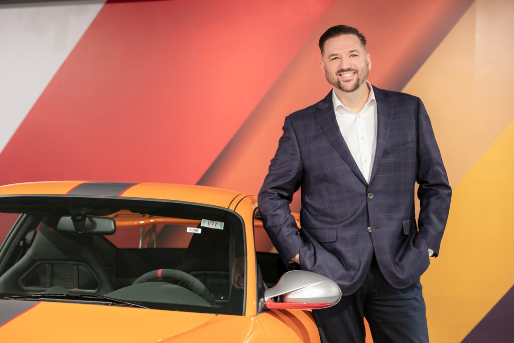 Environmental executive portrait of a businessman photographed beside a sports car