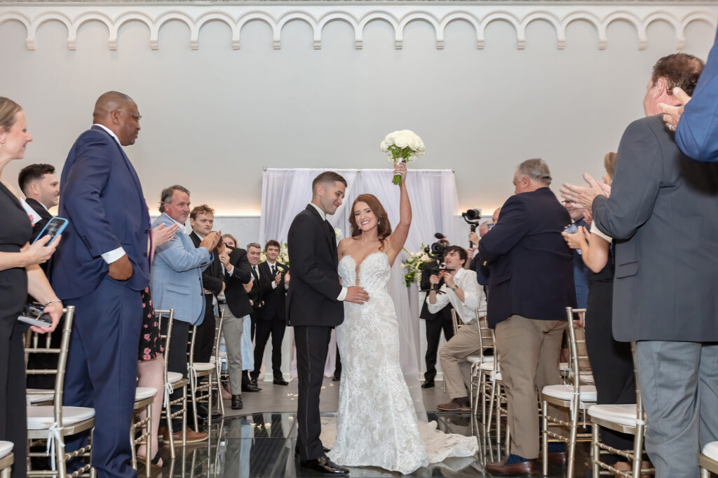 Bride and groom leaving their wedding ceremony as the bride raises her bouquet at Limestone Hall in Lexington, Kentucky